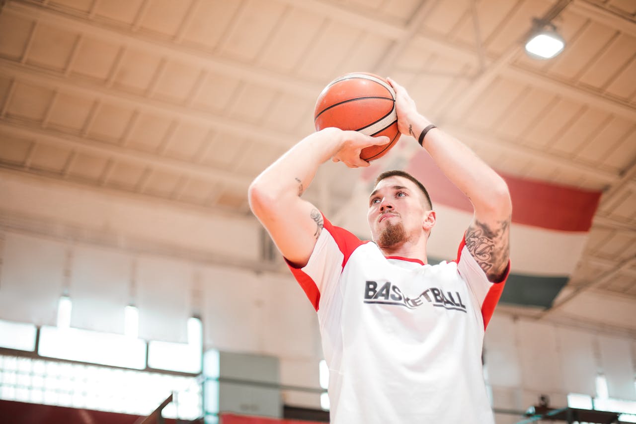 From below of concentrated basketball player with tattoos on arms preparing throwing ball to hoop